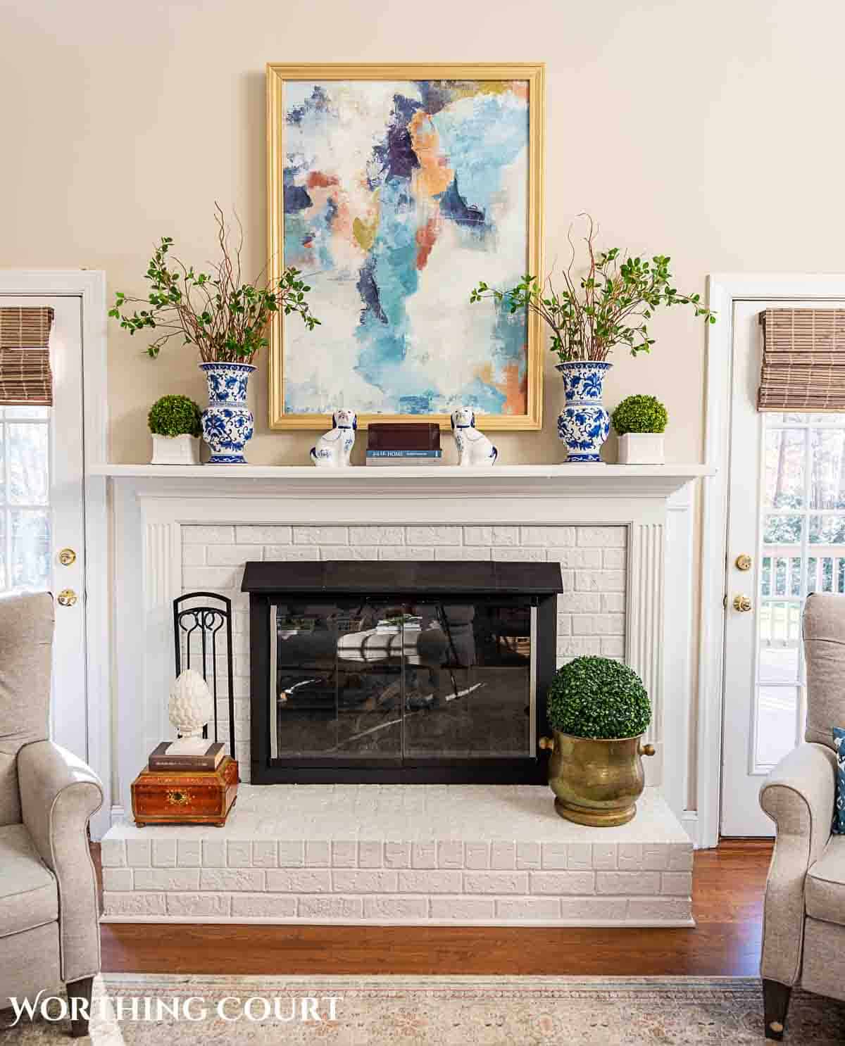 white brick fireplace with art above and a decorated mantle.