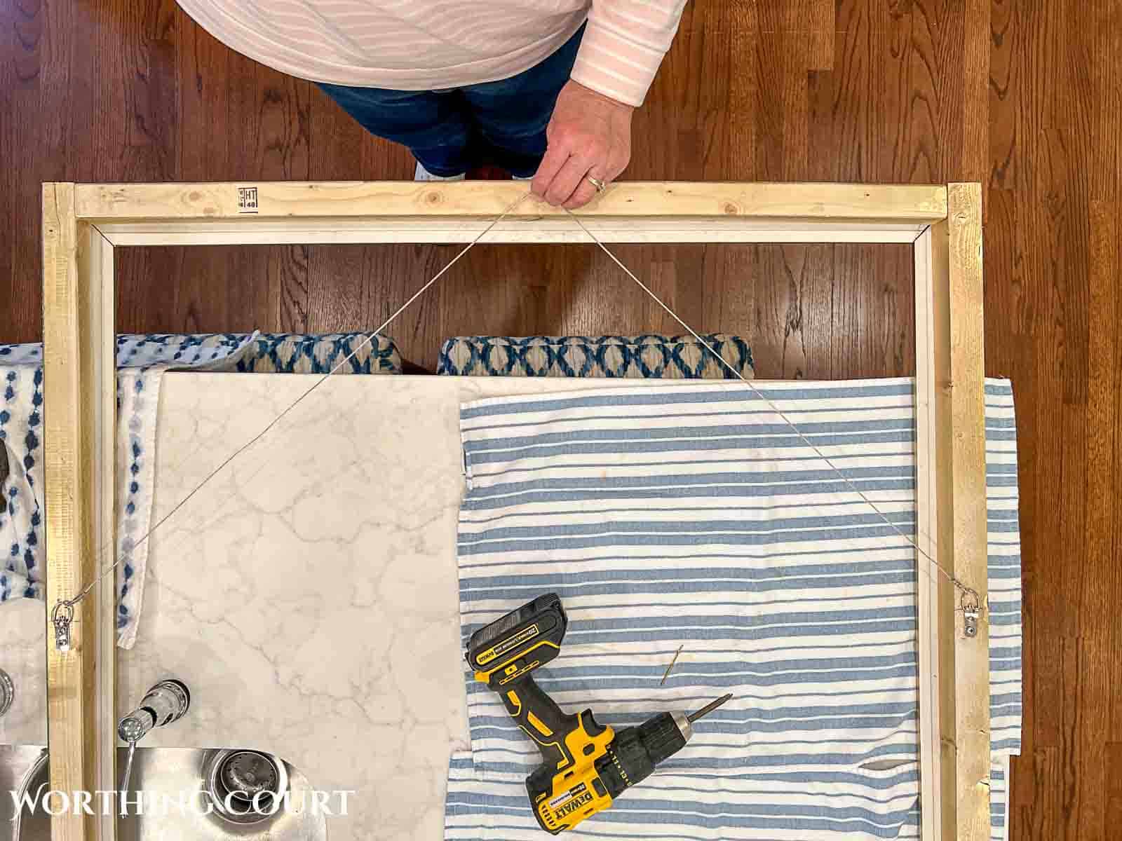 person pulling on hanging wire to check the length for a canvas art frame