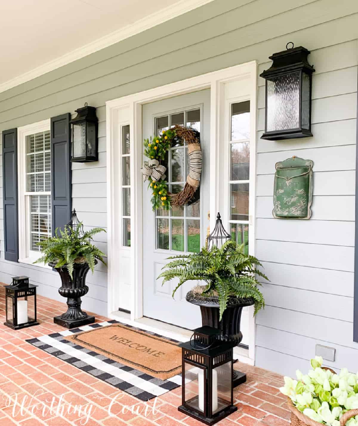 gray front door with ferns in urns and a spring wreath on the door
