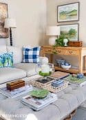 living room with gray couch, upholstered coffee table, wall art above console table and accessories