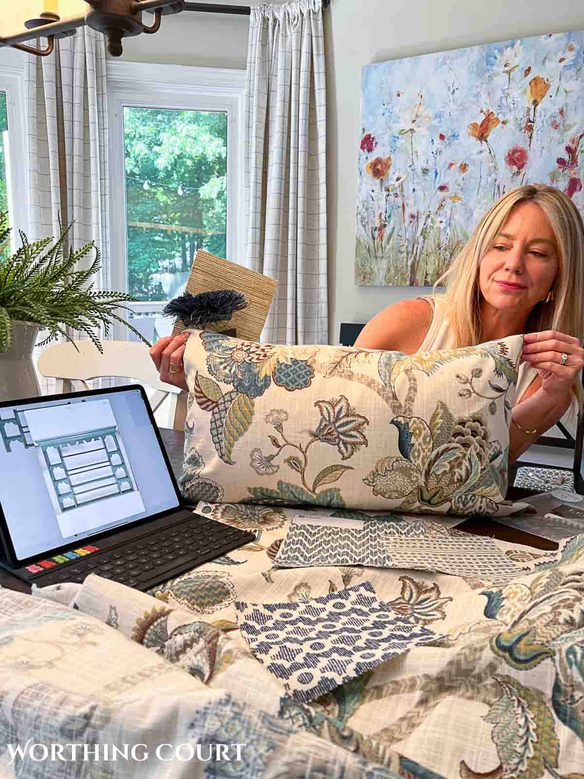 interior designer holding pillow up to computer screen with fabric swatches on table