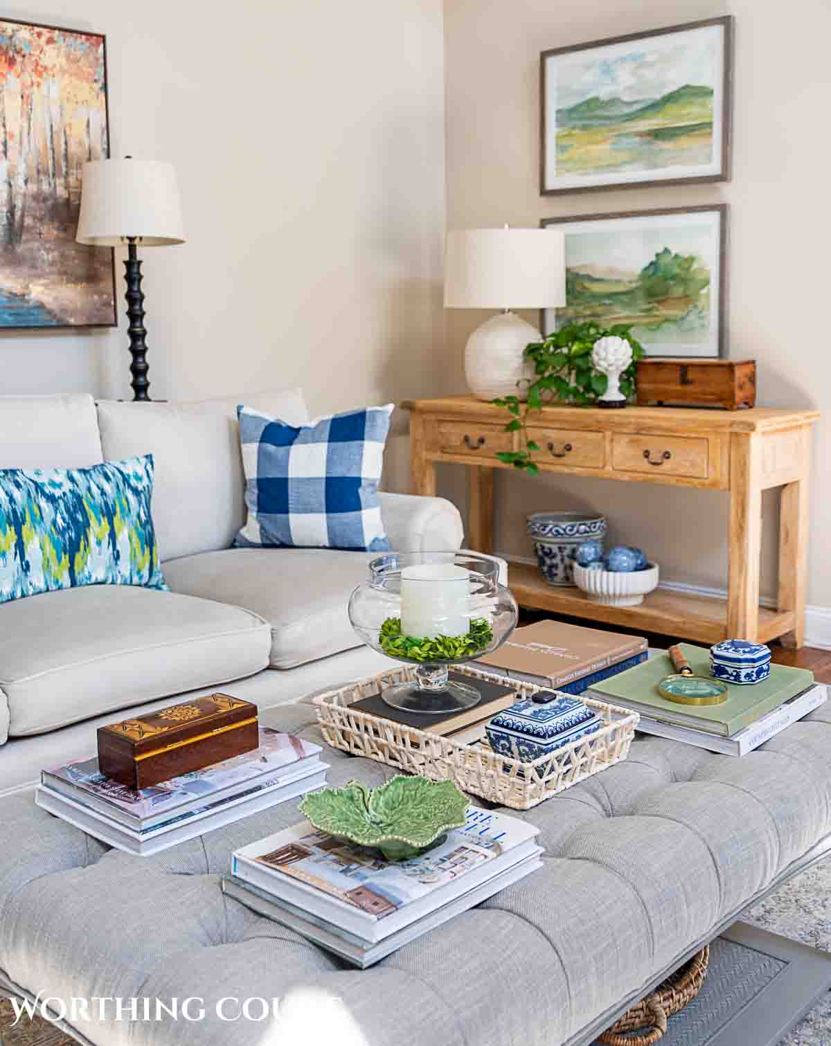 living room with gray couch, upholstered coffee table, wall art above console table and accessories