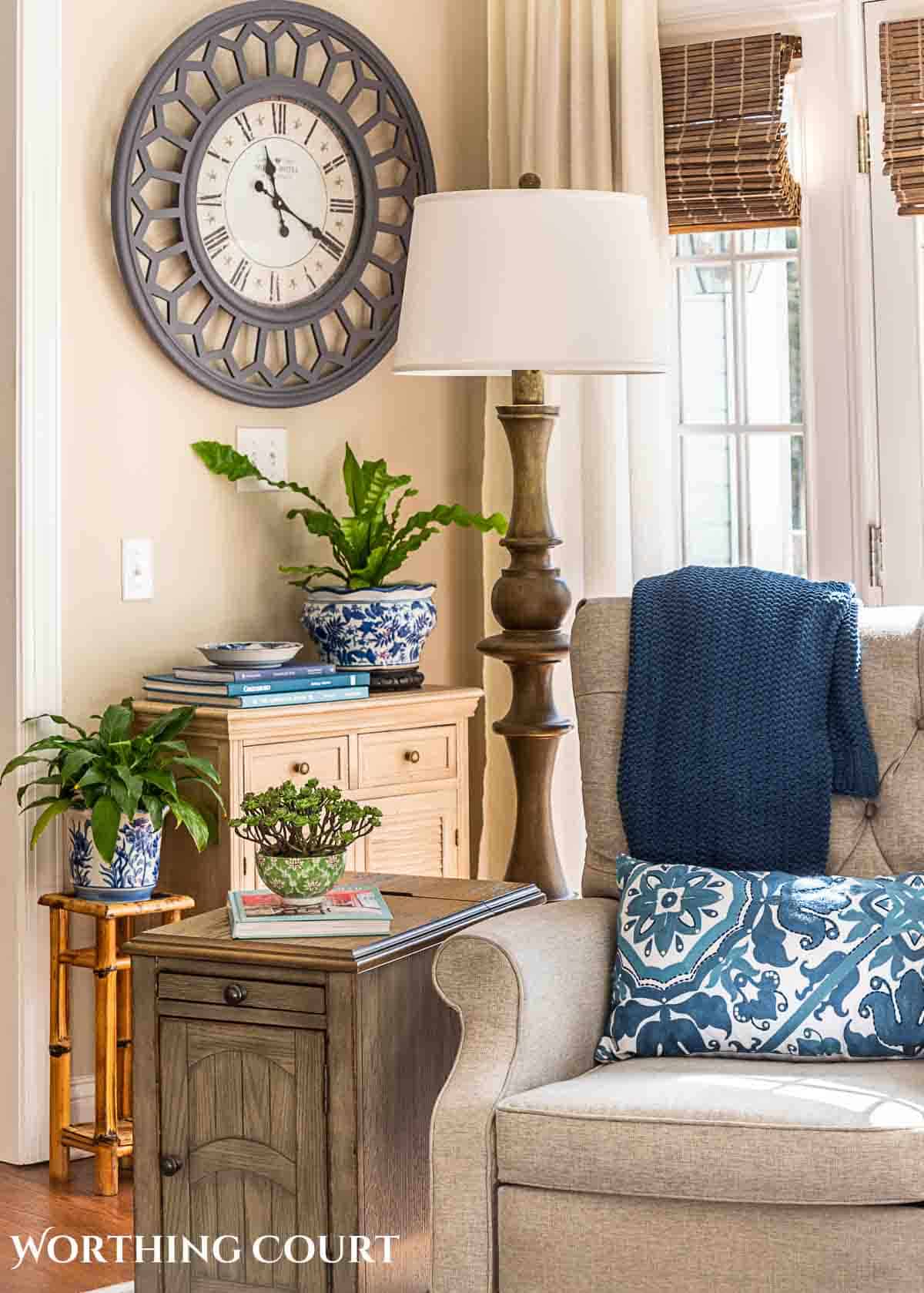 living room wall with large clock for wall art behind gray recliner and end table with accessories