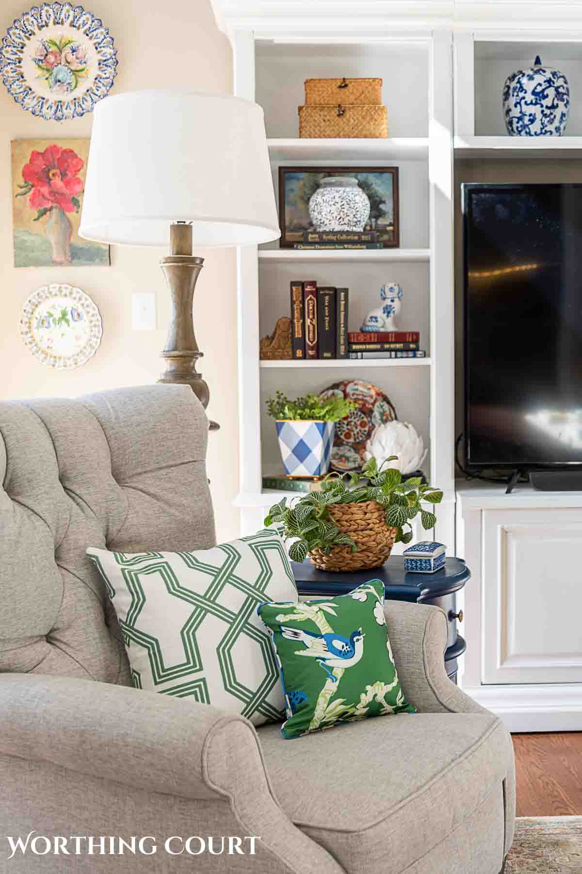 living room entertainment center behind gray arm chair with green pillows