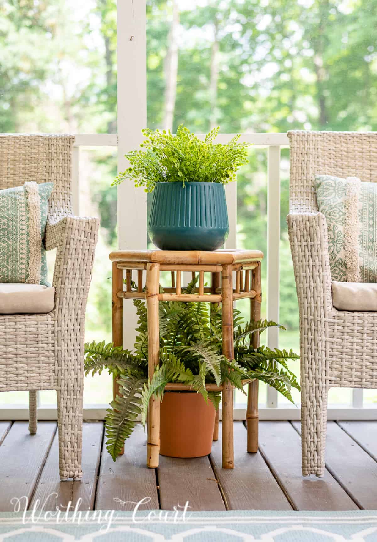bamboo plant stand with plants between two wicker arm chairs
