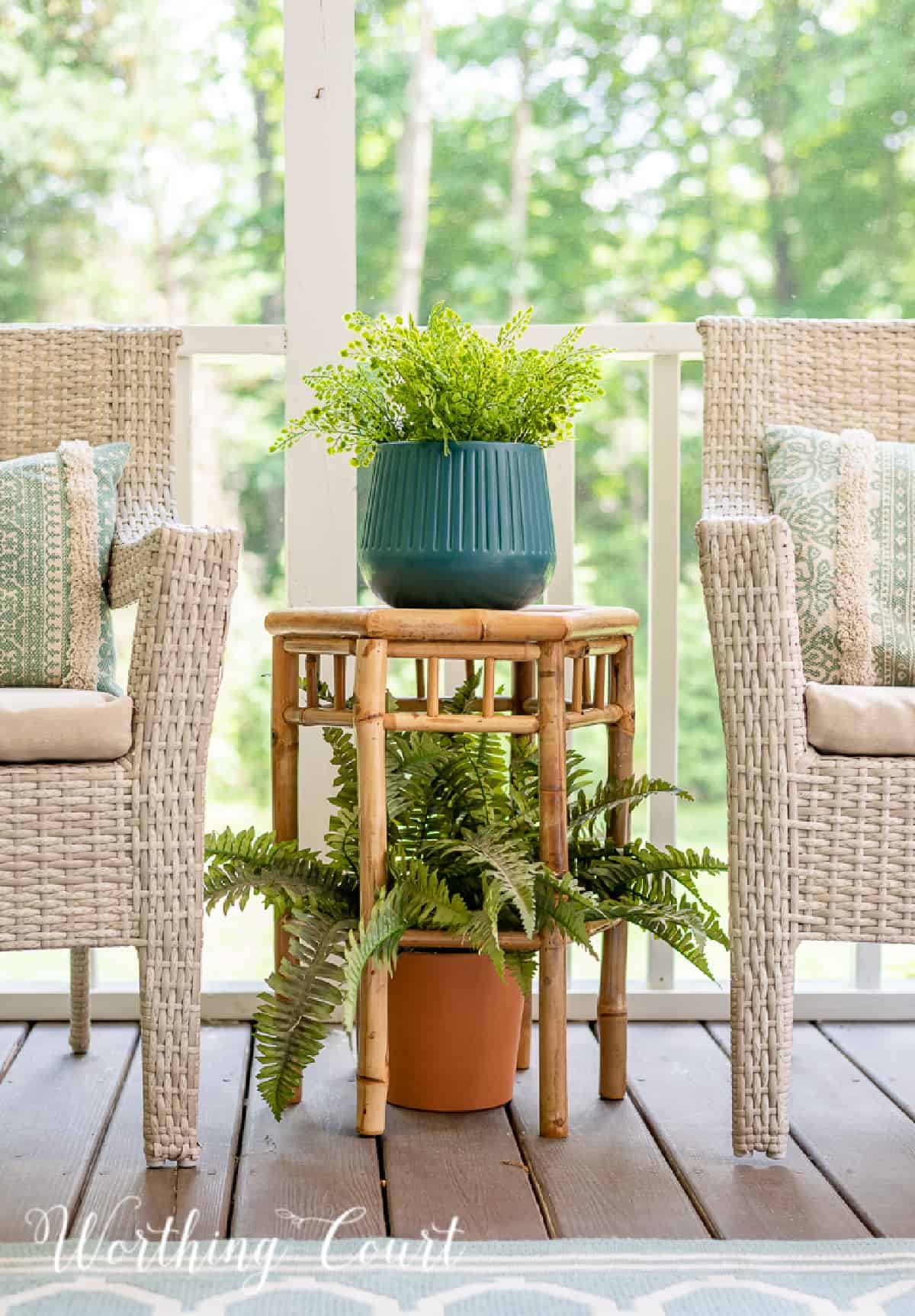 bamboo plant stand with plants between two wicker arm chairs
