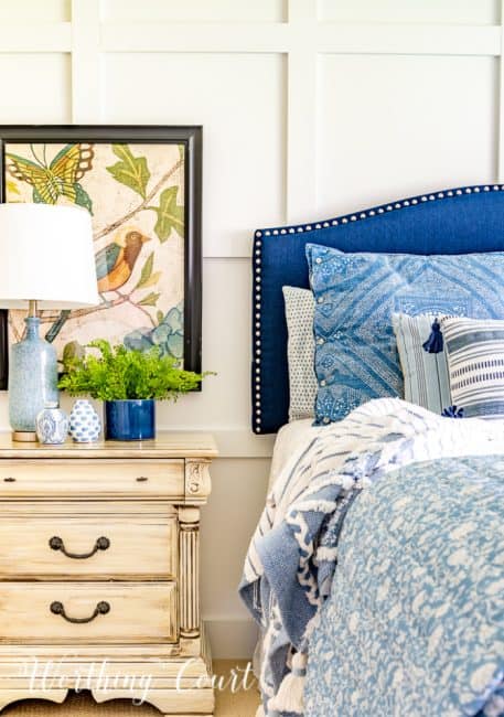 partial image of bed with blue headboard and blue and white bedding and night stand with art
