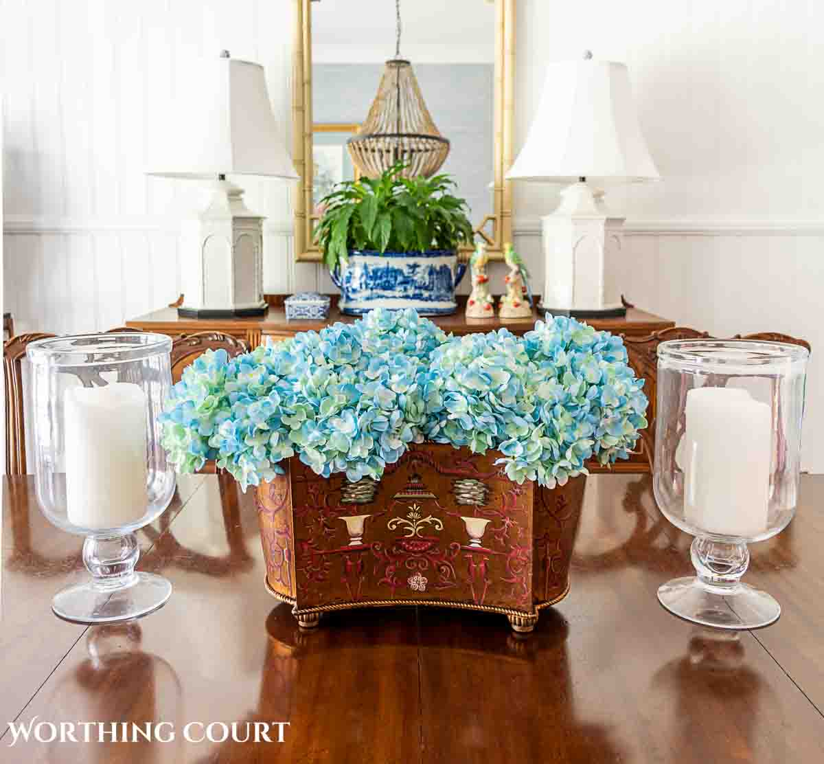 faux blue hydrangeas in an oblong container flanked by candles in hurricanes for as a dining room table centerpiece