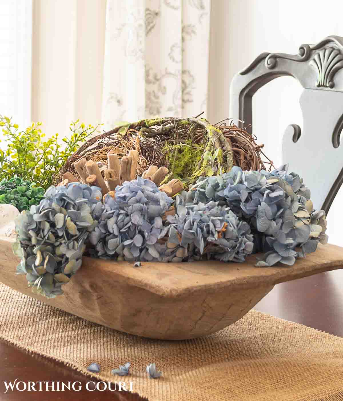 dough bowl filled with greenery, bird, nest and blue hydrangeas used as a centerpiece