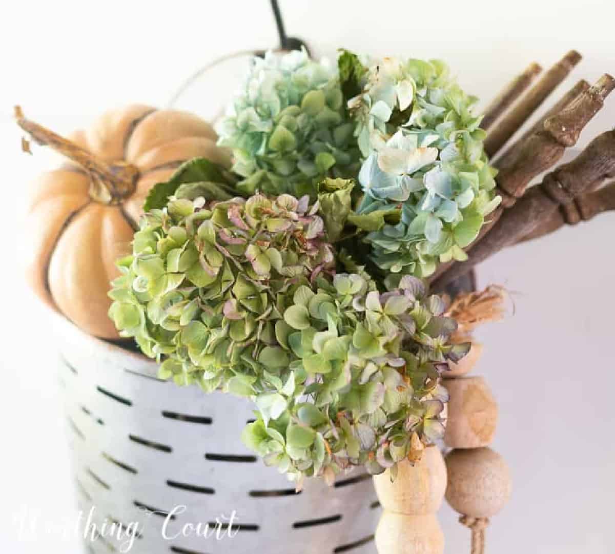 metal basket filled with pumpkins, wood beads, spindles and dried blue hydrangeas