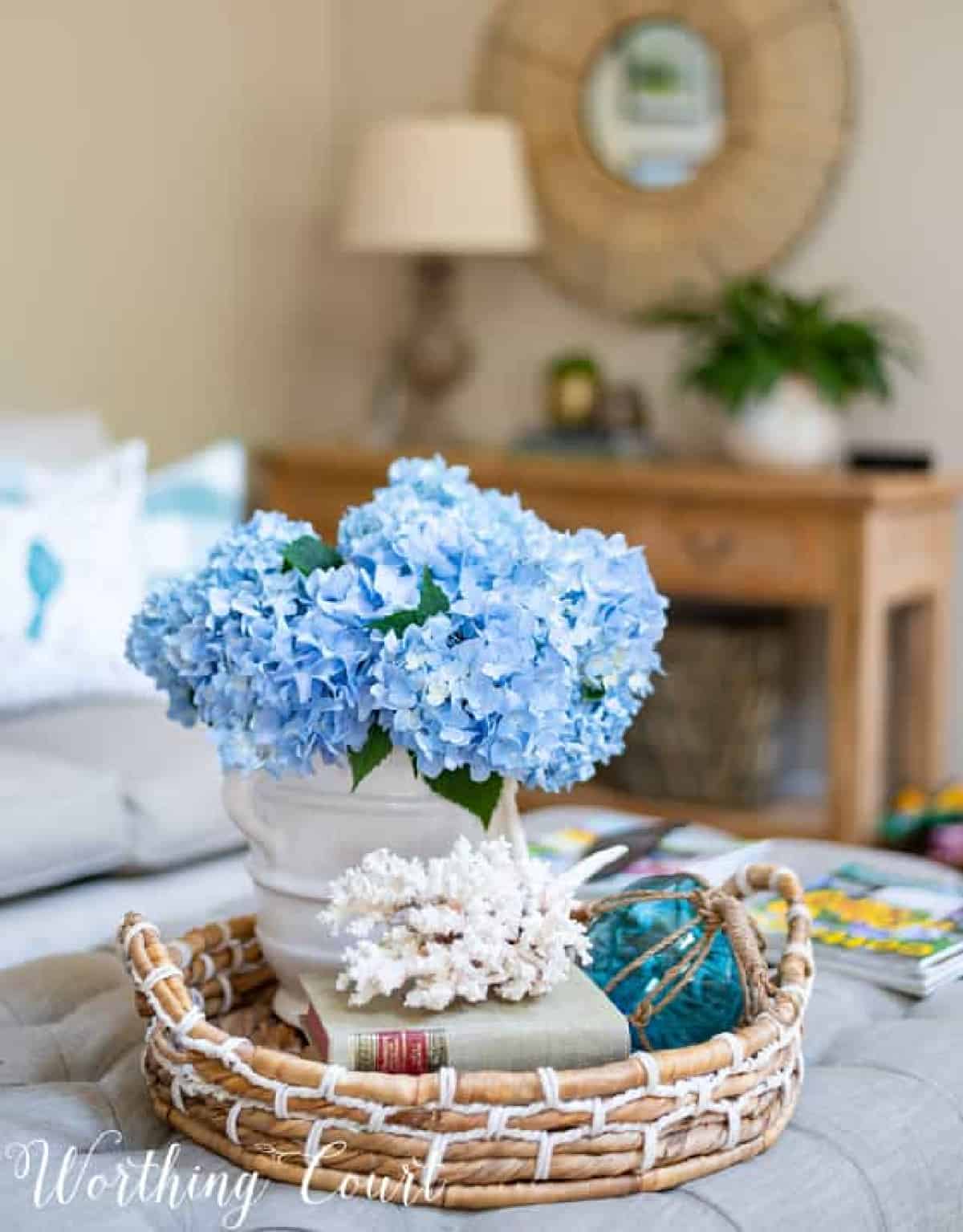 summer vignette with blue hydrangeas in a white vase with coral and a fishing float