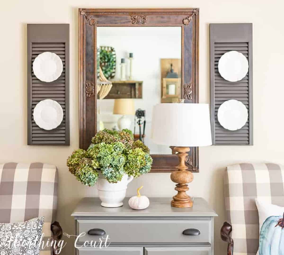 mirror above gray chest, flanked by shutters with lamp and hydrangea arrangement in a white vase