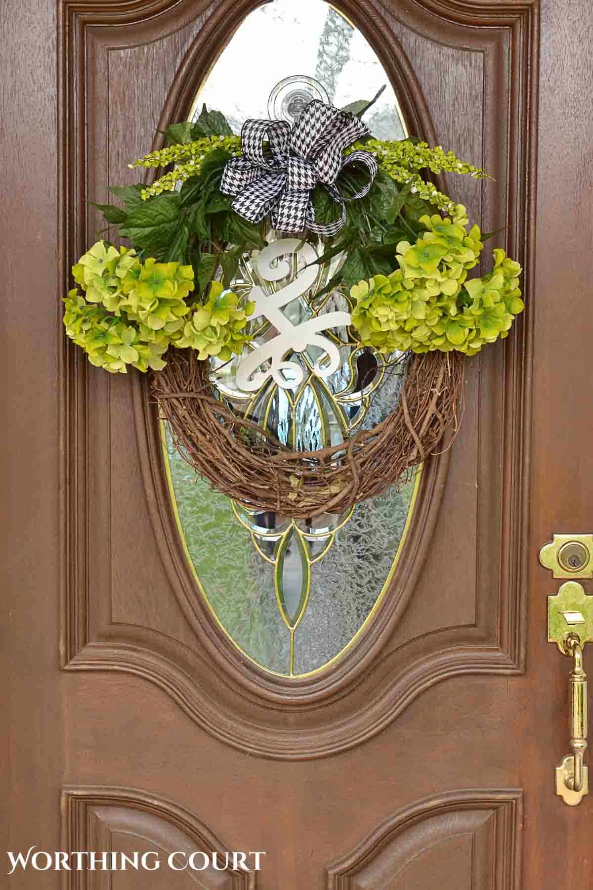 green hydrangea arrangement on a grapevine wreath hanging on a front door