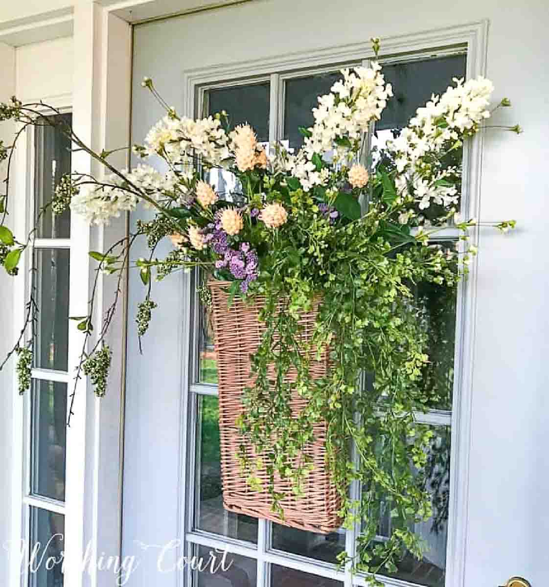basket hanging on front door filled with hydrangeas and other flowers and greenery