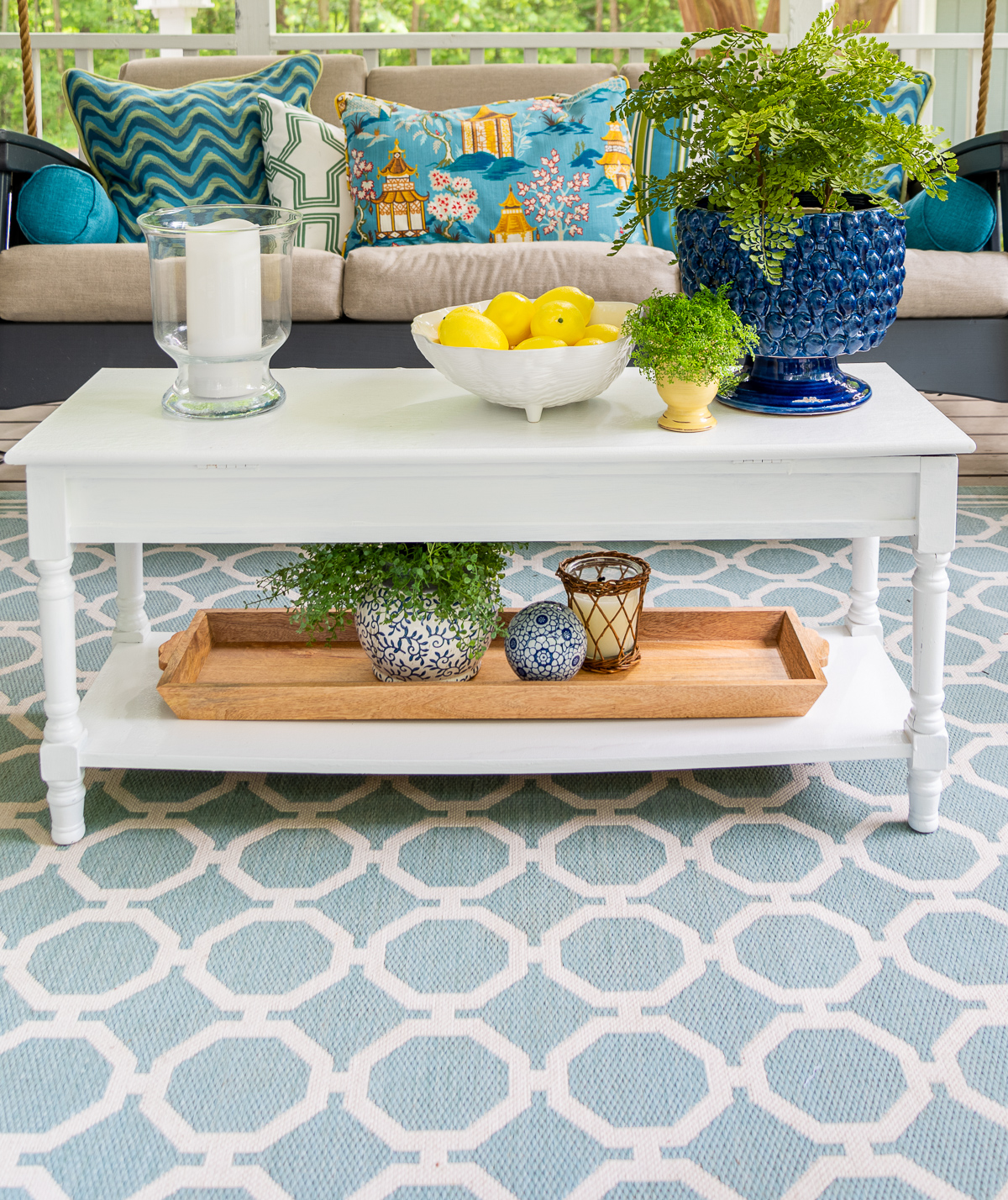 painted white coffee table with blue, white and yellow accessories on an aqua outdoor rug with a lattice pattern