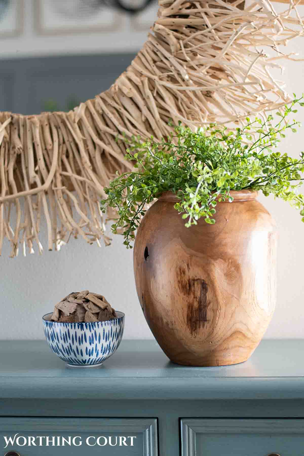 coastal decorating idea featuring a wood vase on a blue chest in front of a mirror with a twig frame