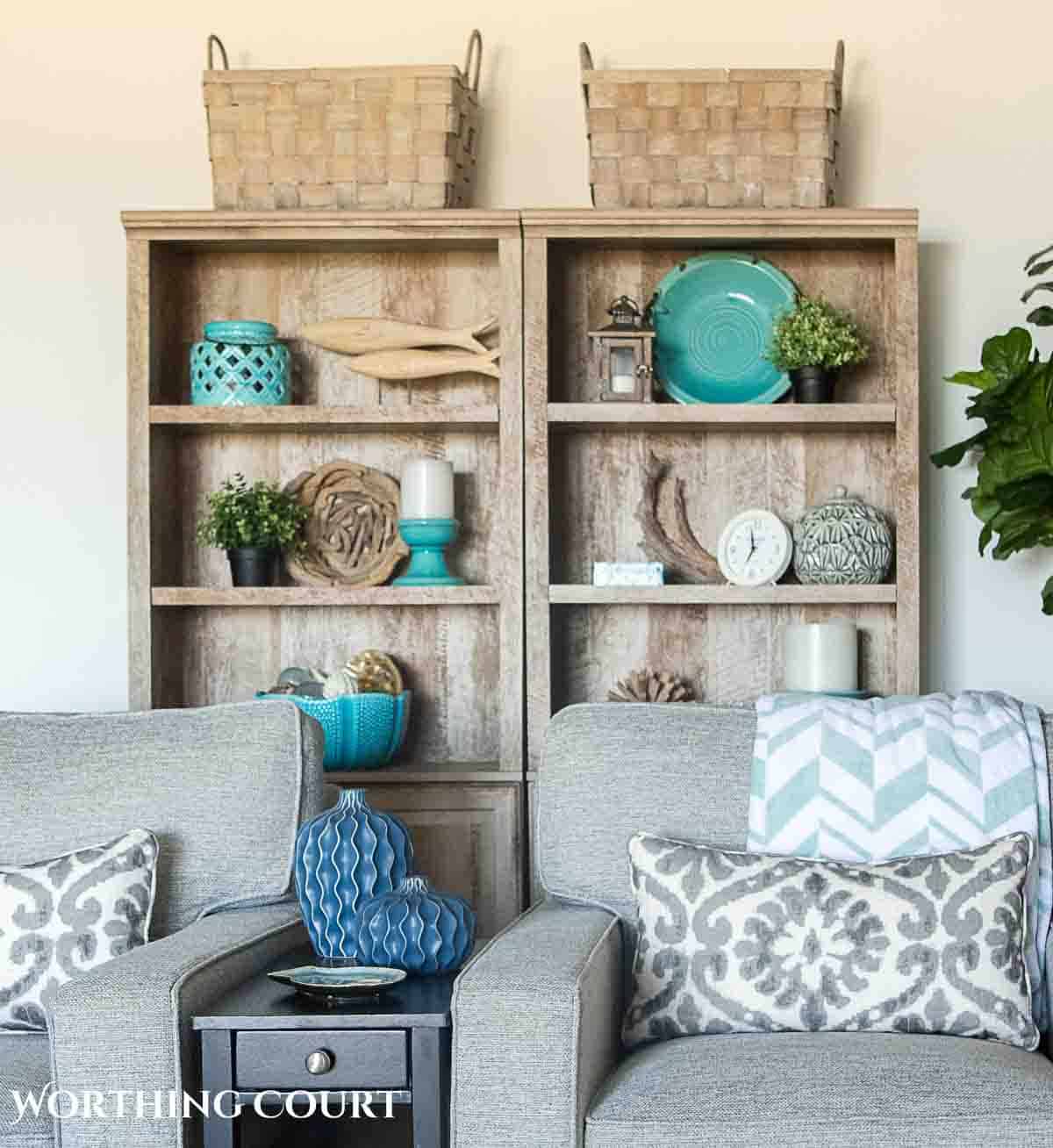 driftwood finish bookcase filled with beach inspired accessories behind two gray arm chairs
