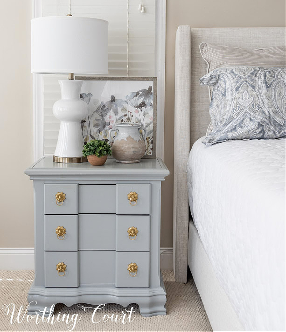 gray nightstand with a white lamp beside a bed with an upholstered headboard