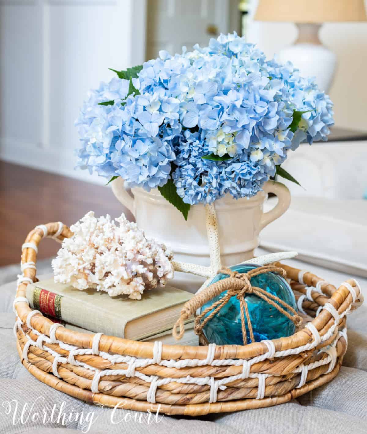 blue hydrangeas in a white vase in a wicker basket with coastal style accessories