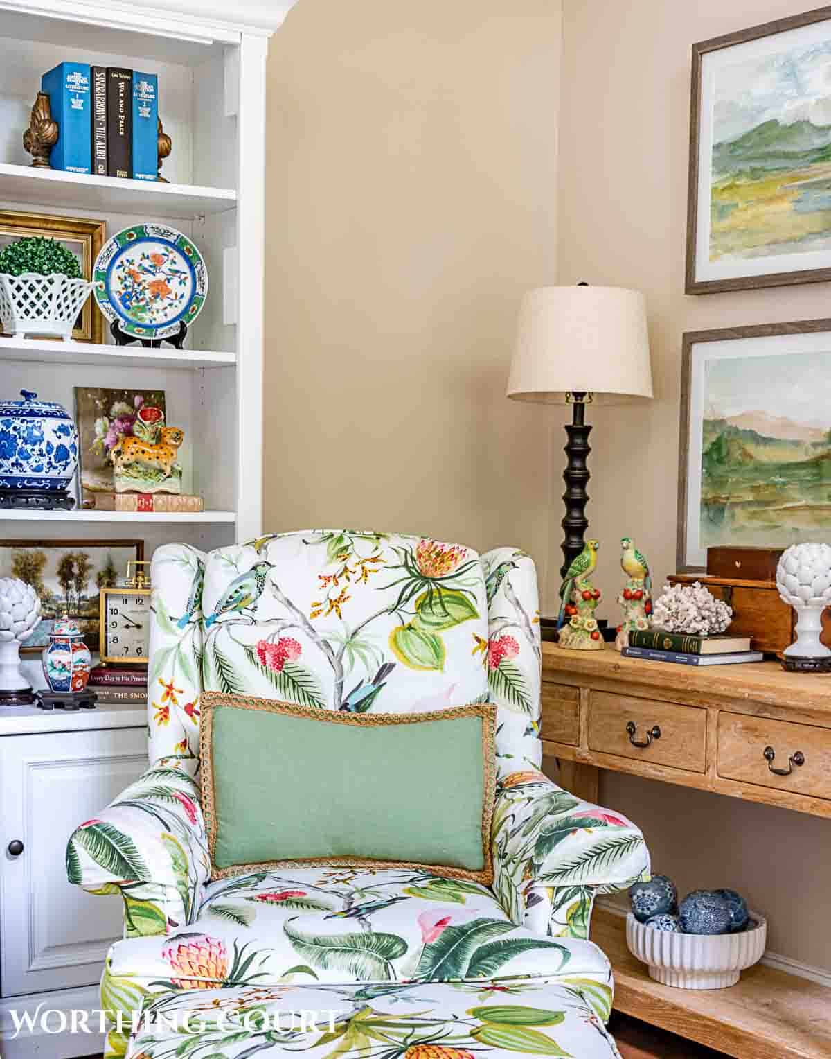 floral upholstered arm chair with green pillow in front of shelves and console table with summer decorations