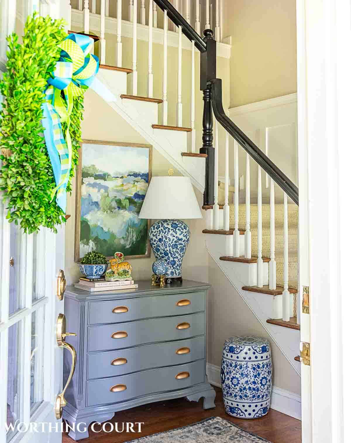 view through front door of a foyer decorated for summer included a gray chest, abstract art and blue and white accessories.