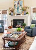 wood coffee table with late summer accessories in front of a white brick fireplace and blue chair