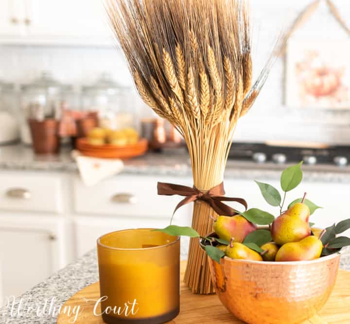 fall kitchen island vignette with a wheat bunch, candle and faux pears in a copper bowl