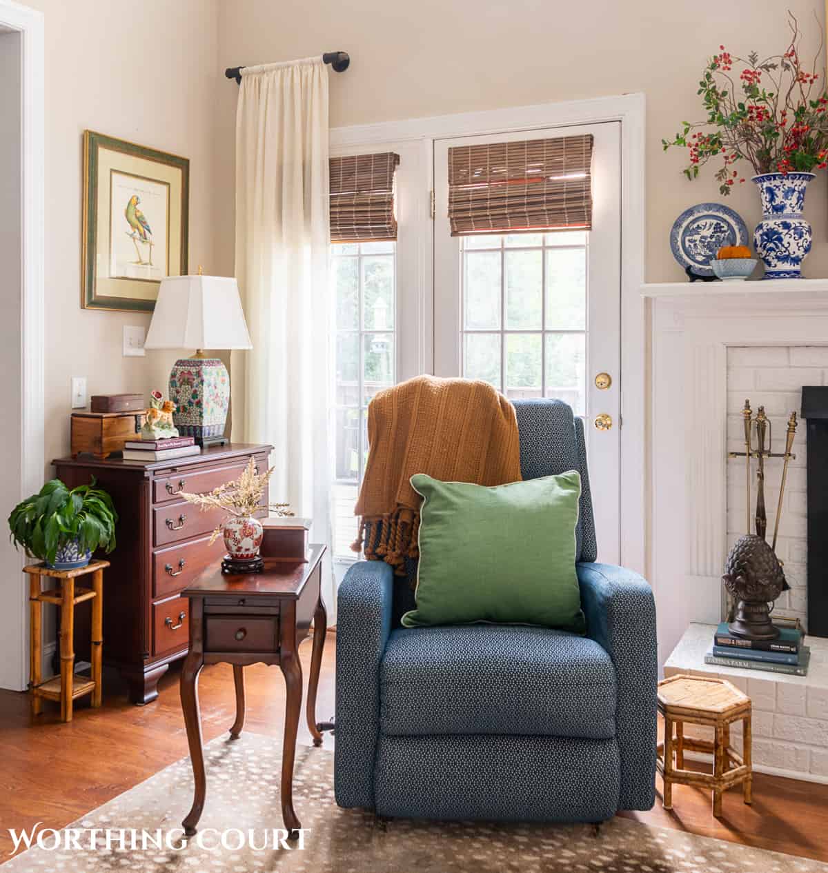 blue arm chair in front on french doors beside small table and chest with lamp