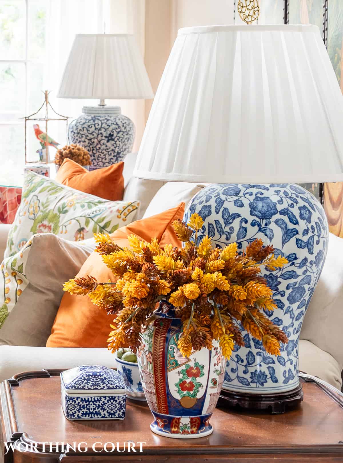 blue and white lamp and a vase filled with fall stems on a brown wood end table