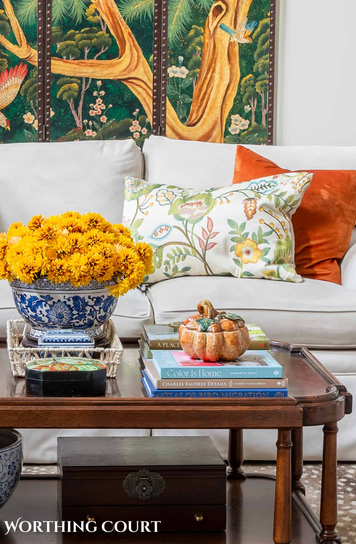 decorative wall screen hanging above a beige couch with fall throw pillows and a brown wood coffee table with fall decorations