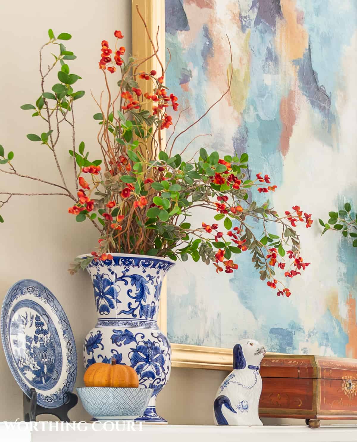 faux fall leaf stems in a blue and white vase on a white mantel