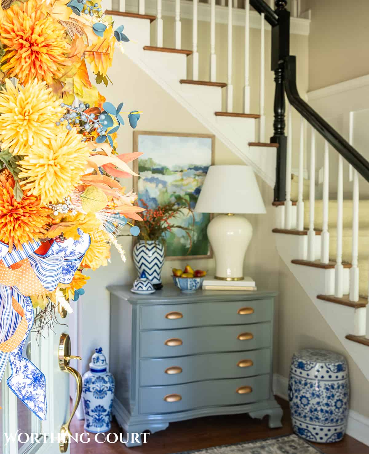 blue and white ginger jar with faux fall stems and a bowl of fake pears beside a white lamp on a gray chest