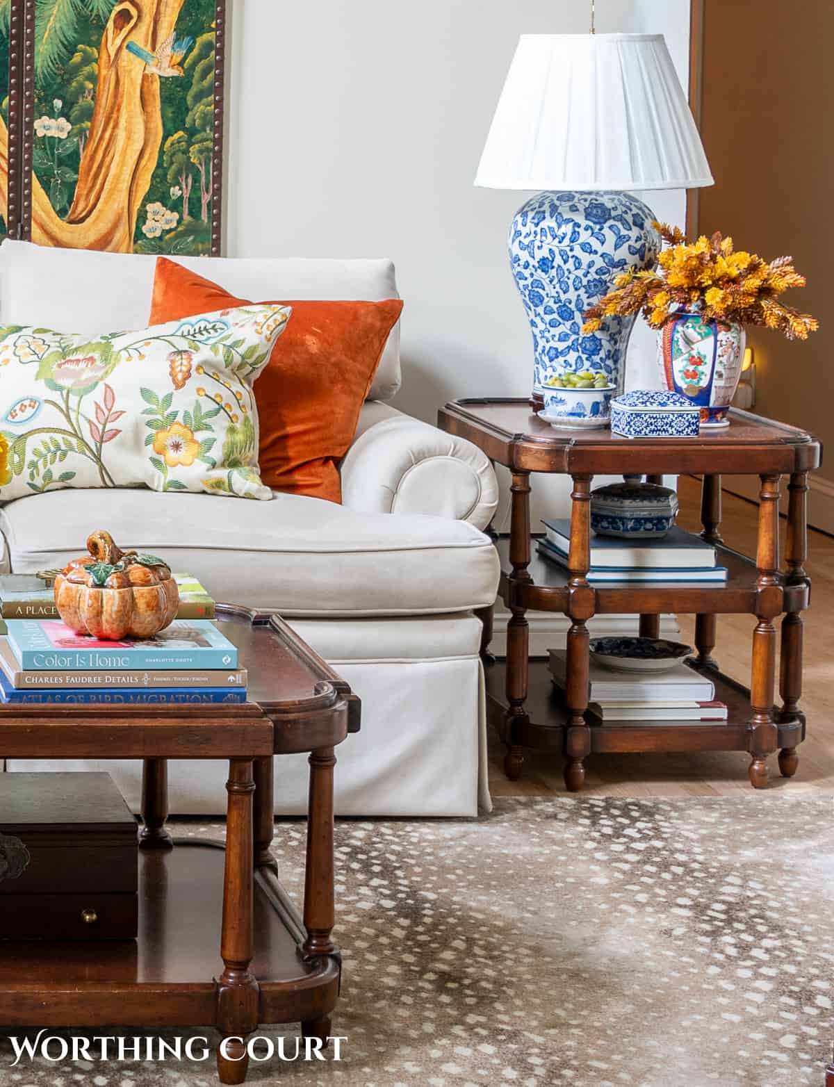 partial view of a coffee table and an end table with a blue and white lamp at the end of a beige couch with fall decorations