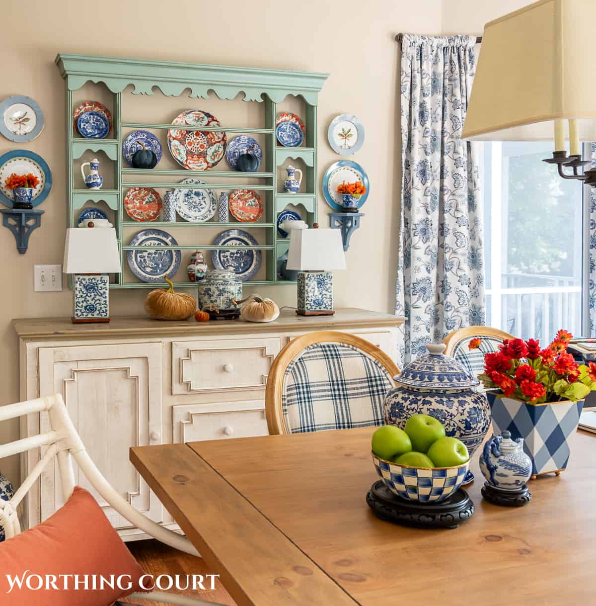 plate rack above a white sideboard filled with blue and white dishes and orange dishes for fall and a fall centerpiece on the dining table