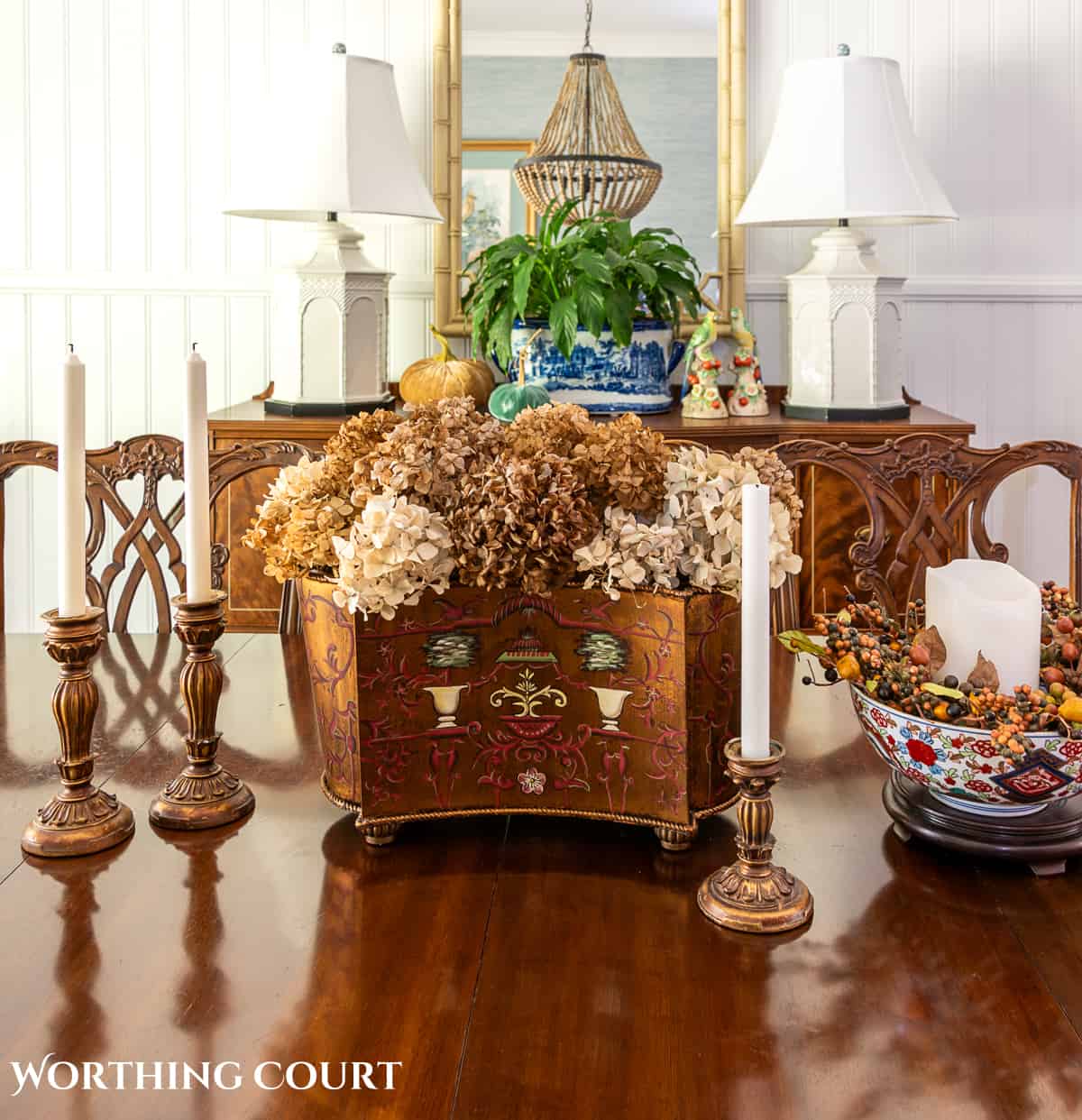 fall centerpiece on a dining table with dried hydrangeas in a brown cachepot flanked by gold candlesticks