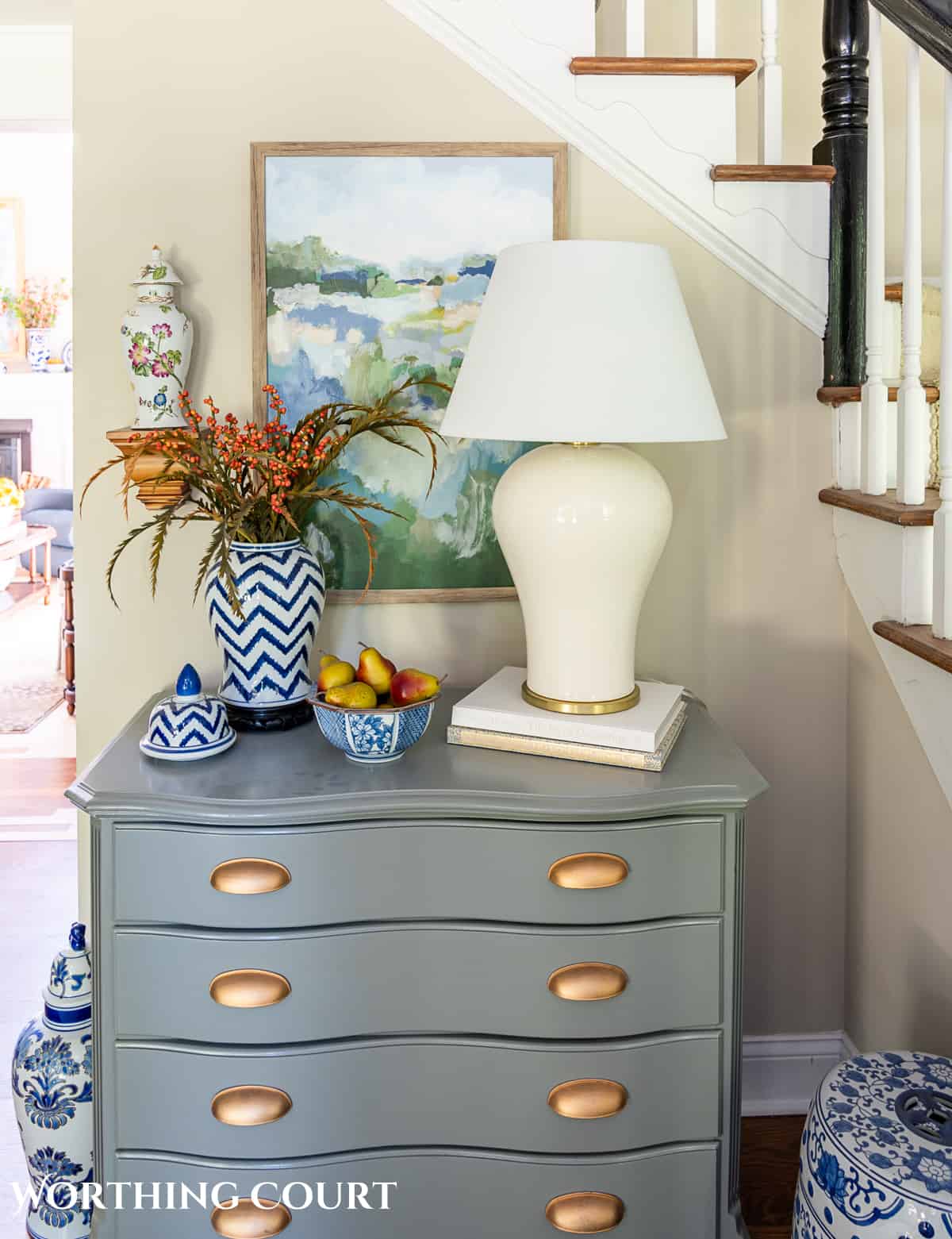 gray chest topped with a blue and white vase filled with fall stems and a white ginger jar shaped lamp