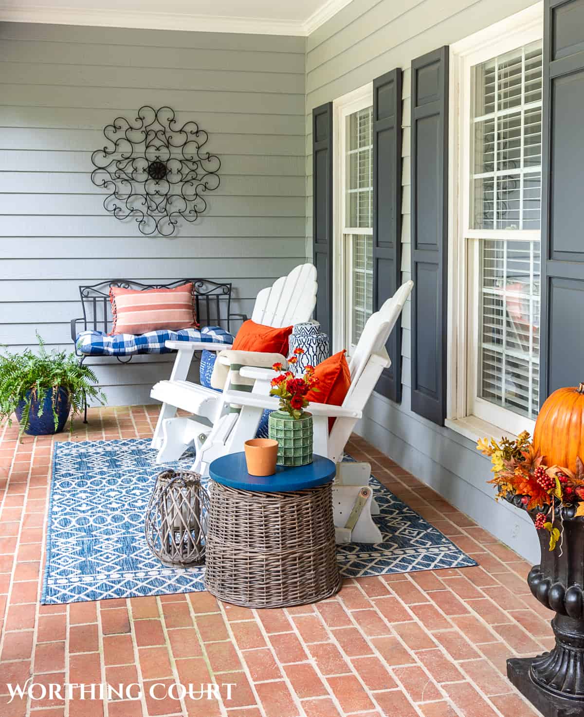 seating area on a large front porch decorated for fall with white gliders and other accessories