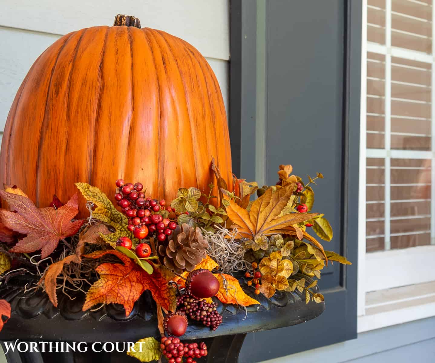 large pumpkin in a planter surrounded with fall picks on a large front porch decorated for fall