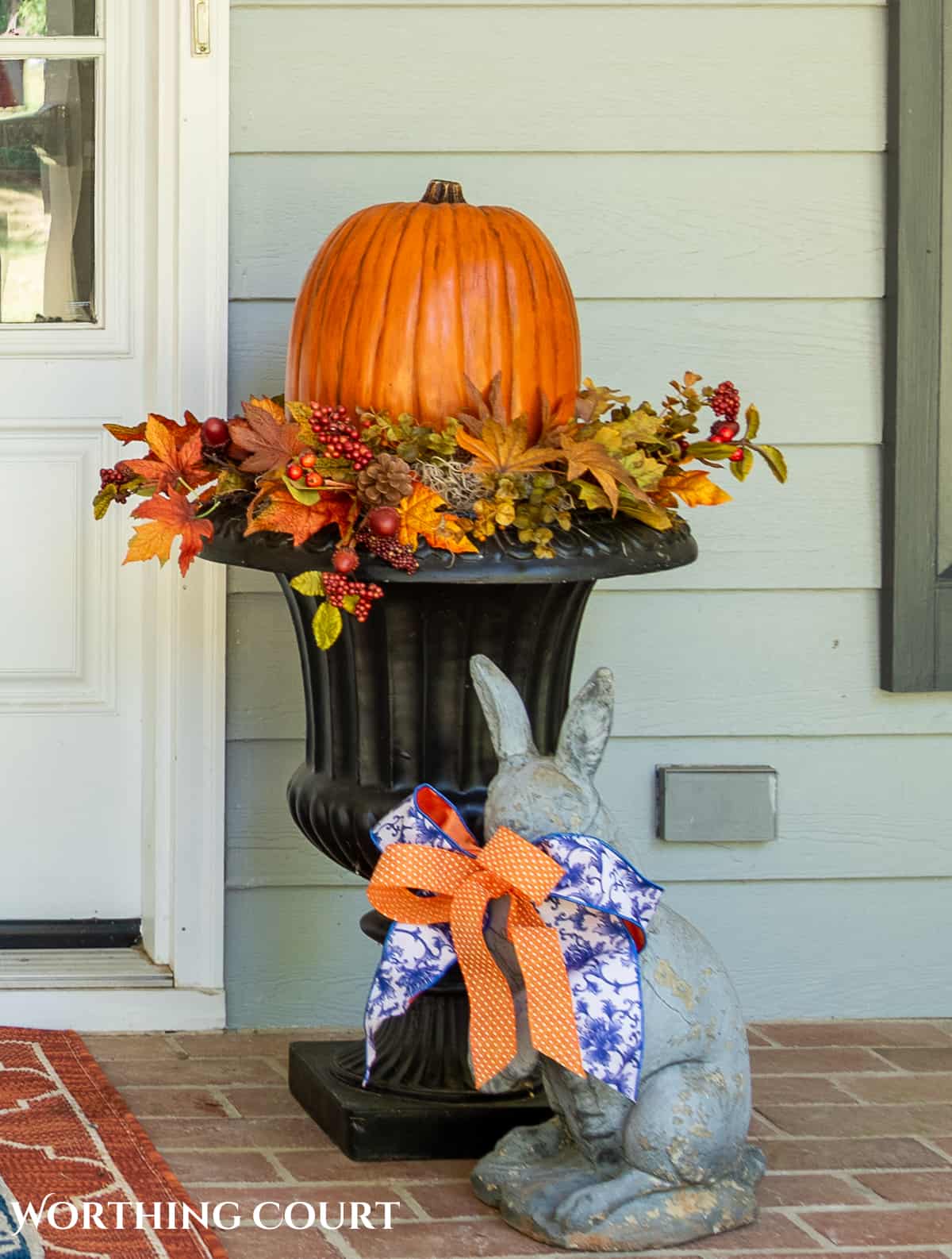 large pumpkin in a planter surrounded with fall picks on a large front porch decorated for fall