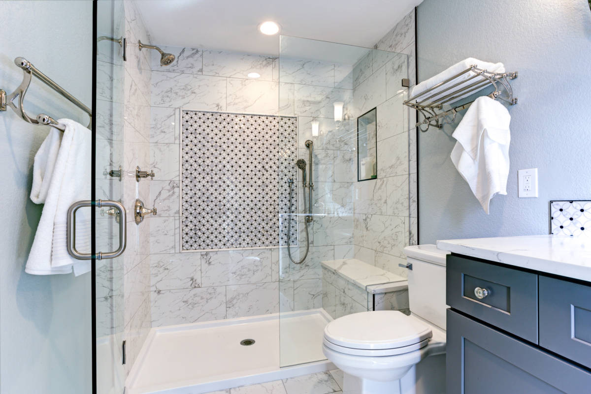 looking into a shower with gray and white tile on the wall and glass shower door