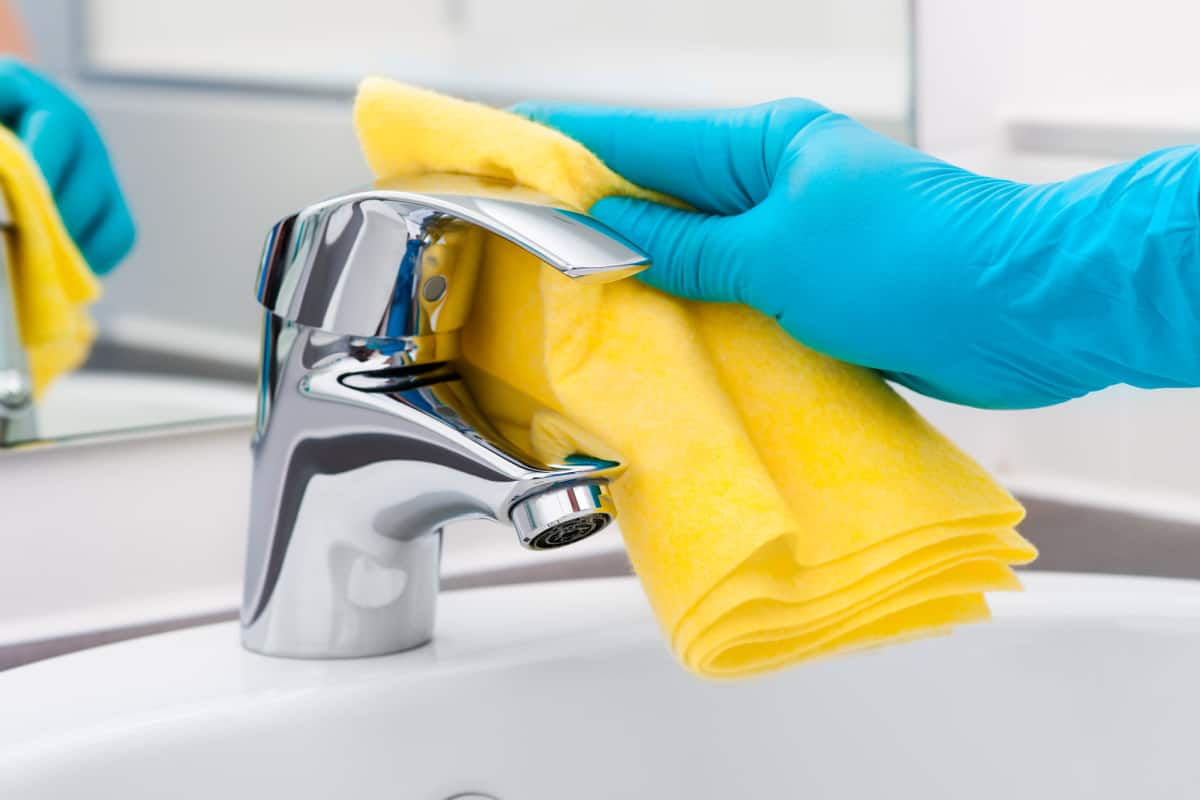 person's hand in a blue rubber glove cleaning a bathroom faucet