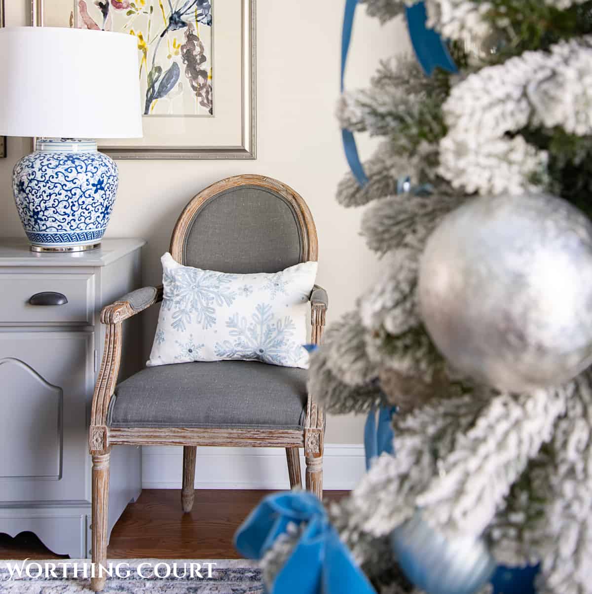 gray dining chair beside gray chest with blue and white lamp with a Christmas tree in the foreground