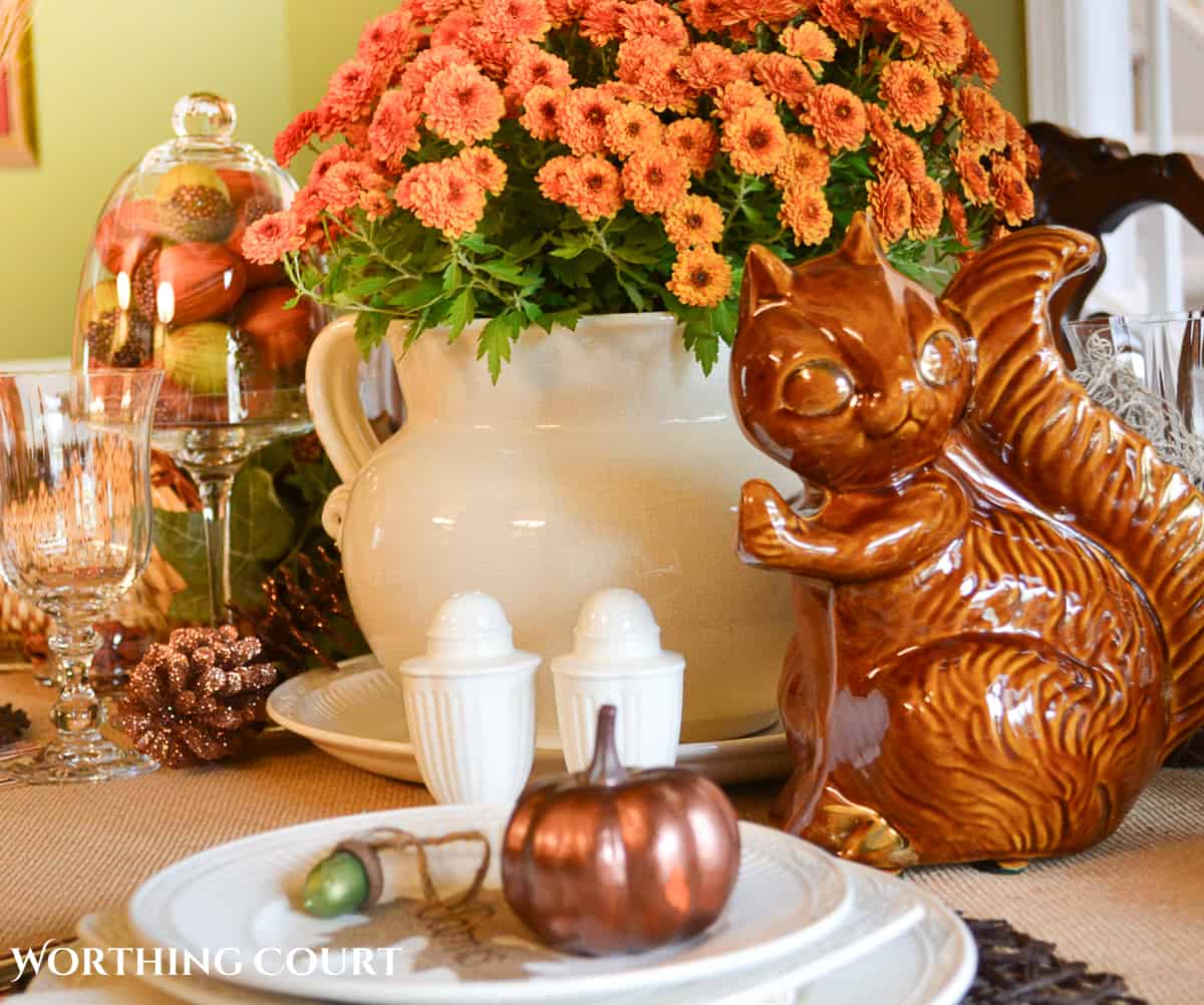 Woodland themed Thanksgiving table setting with fall colored mums, a cornucopia, ceramic squirrel and white dishes