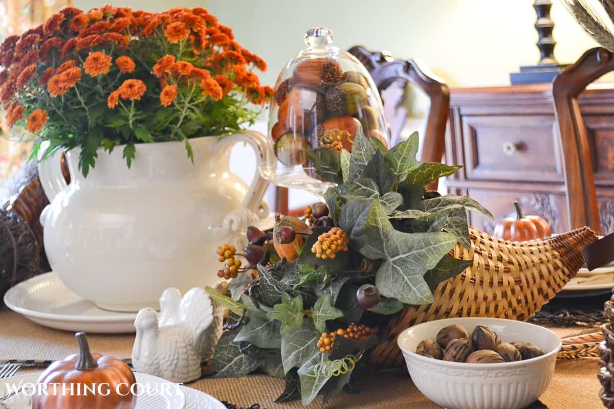 Woodland themed Thanksgiving table setting with fall colored mums, a cornucopia, ceramic squirrel and white dishes