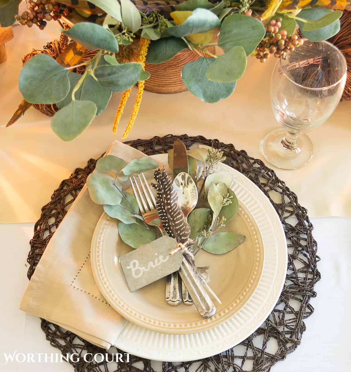 Thanksgiving tablescape designed with neutral linens, white plates, dried eucalyptus and brown glass bottles