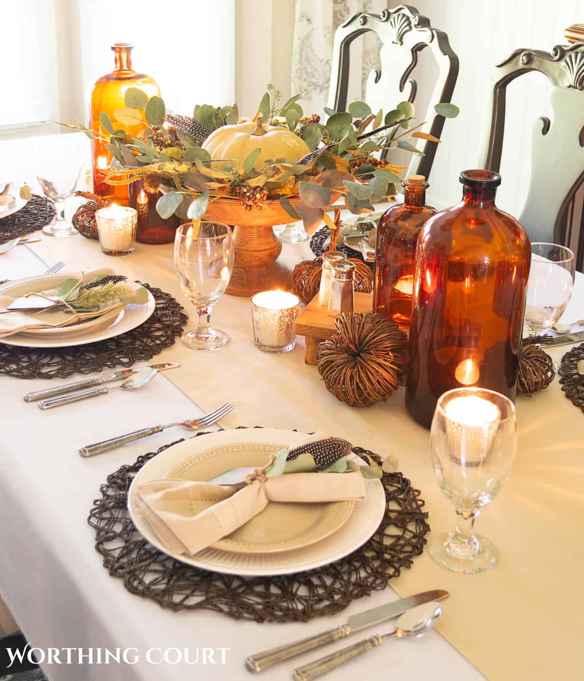 Thanksgiving tablescape designed with neutral linens, white plates, dried eucalyptus and brown glass bottles
