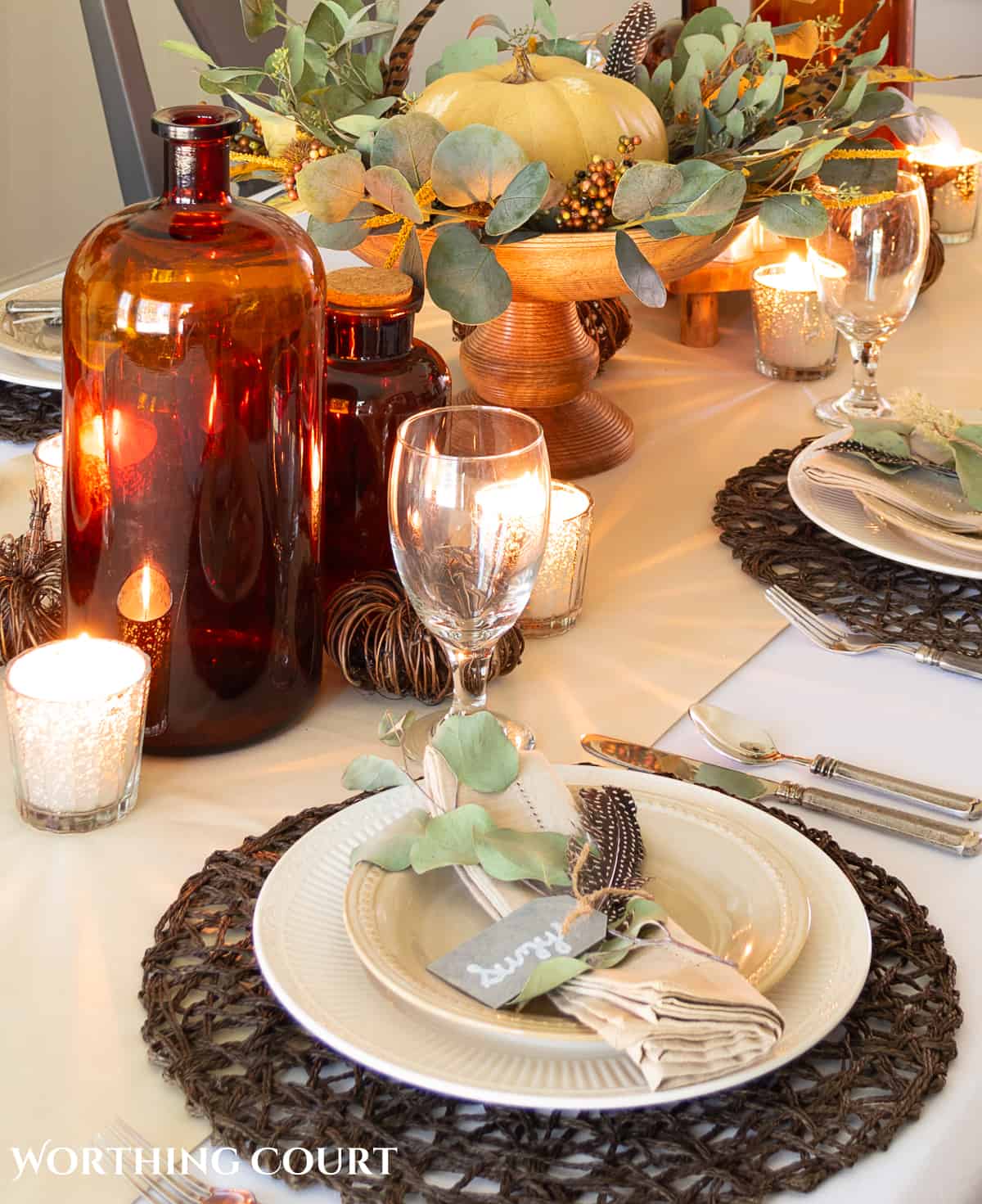 Thanksgiving tablescape designed with neutral linens, white plates, dried eucalyptus and brown glass bottles