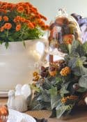 Woodland themed Thanksgiving table setting with fall colored mums, a cornucopia, ceramic squirrel and white dishes