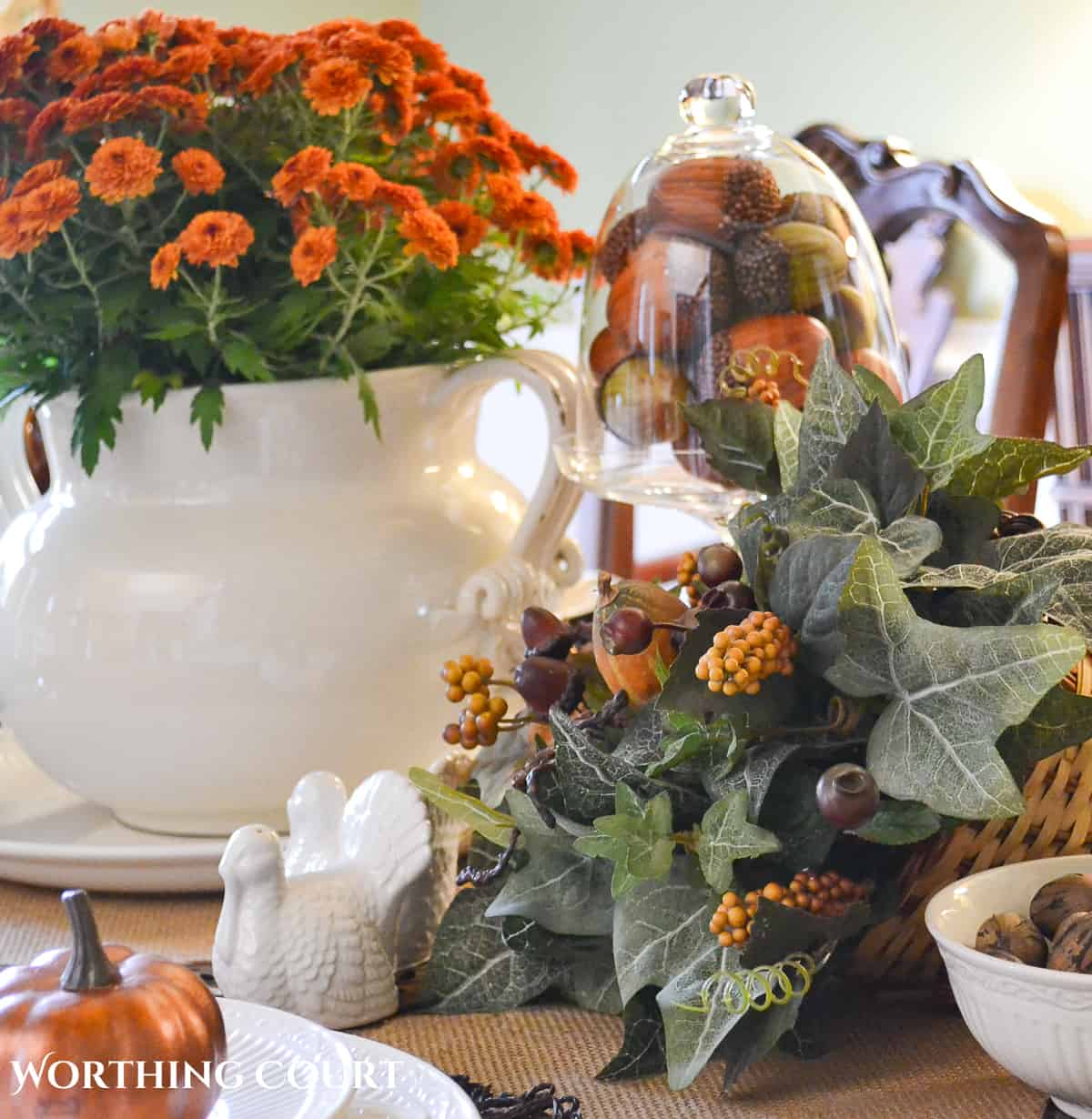 Woodland themed Thanksgiving table setting with fall colored mums, a cornucopia, ceramic squirrel and white dishes