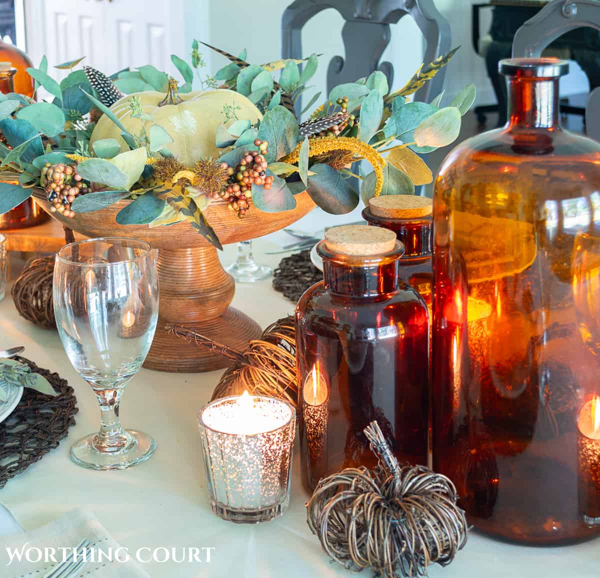 Thanksgiving tablescape designed with neutral linens, white plates, dried eucalyptus and brown glass bottles